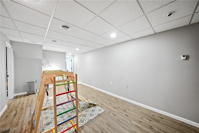 interior space with a paneled ceiling, visible vents, radiator heating unit, wood finished floors, and baseboards