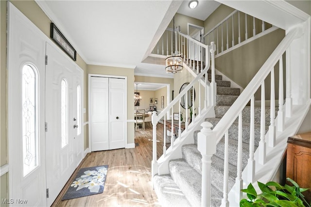 entrance foyer with stairway, light wood-style flooring, a chandelier, and ornamental molding