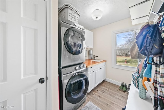 laundry area featuring light wood-style flooring, stacked washer and dryer, a sink, baseboards, and cabinet space