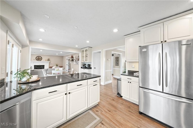 kitchen featuring light wood finished floors, dark stone countertops, stainless steel appliances, a fireplace, and white cabinetry