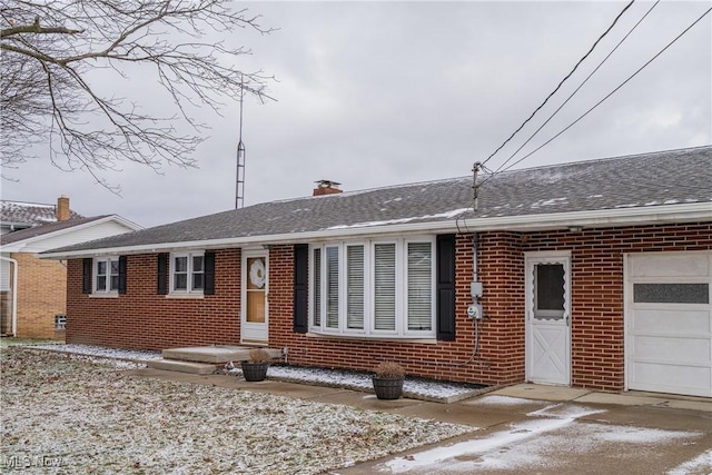 ranch-style house with brick siding, a chimney, an attached garage, and roof with shingles