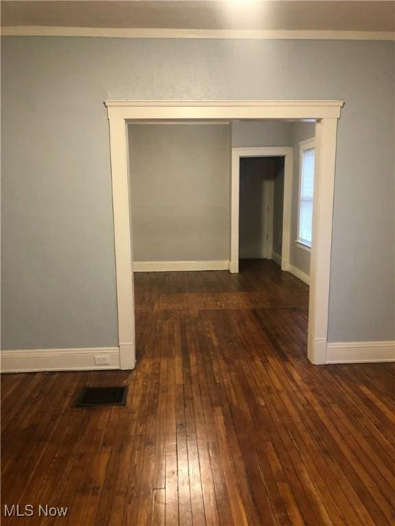 unfurnished room with baseboards, visible vents, dark wood-type flooring, and ornamental molding