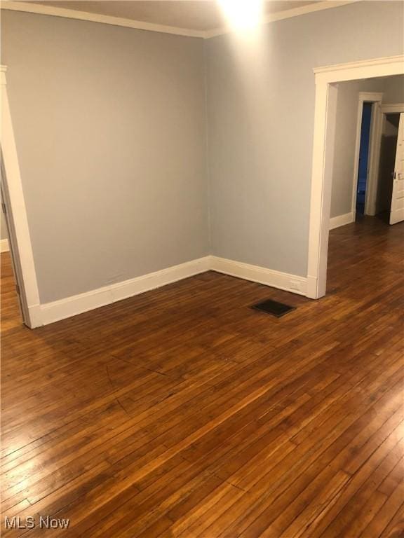 empty room featuring ornamental molding, dark wood-style flooring, visible vents, and baseboards