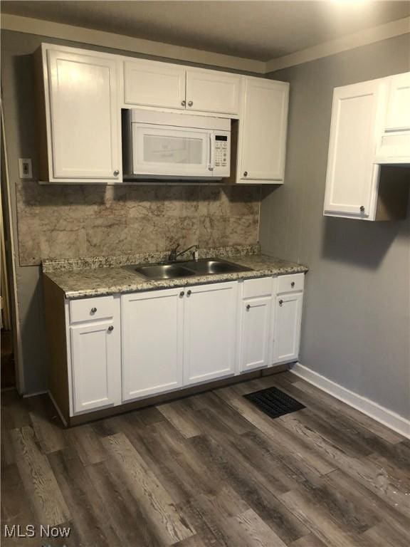 kitchen with dark wood-style flooring, decorative backsplash, white microwave, white cabinets, and a sink