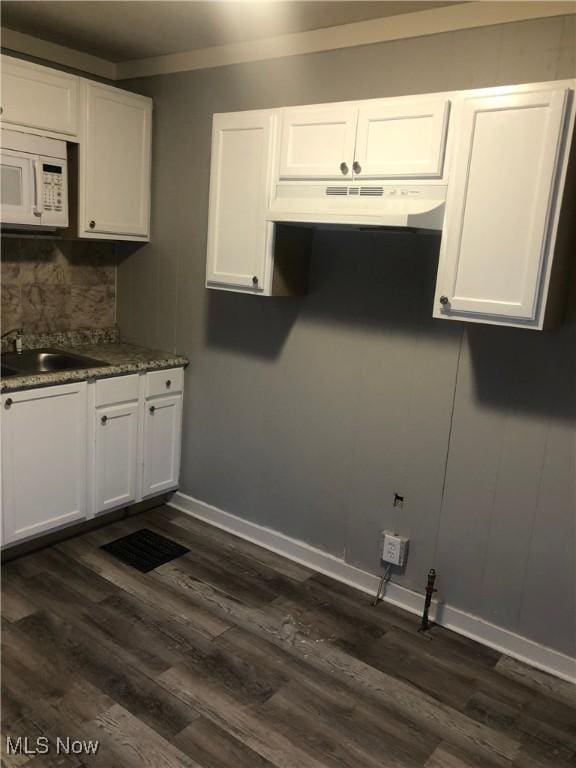 kitchen featuring white cabinetry, a sink, under cabinet range hood, and white microwave