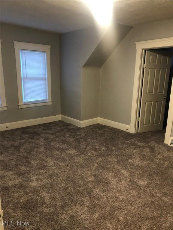 additional living space featuring dark carpet and baseboards