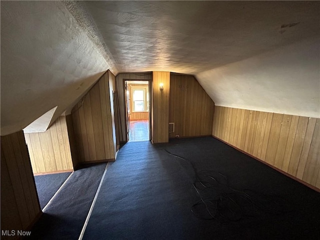 additional living space featuring lofted ceiling, wood walls, a textured ceiling, and dark colored carpet