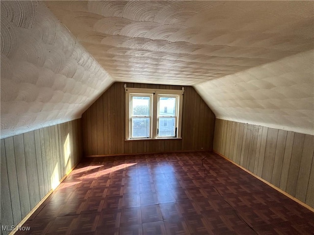 bonus room with vaulted ceiling, a textured ceiling, and wooden walls