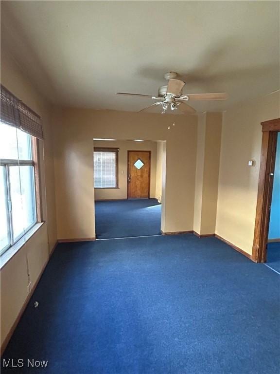 unfurnished room featuring baseboards, dark colored carpet, and a ceiling fan