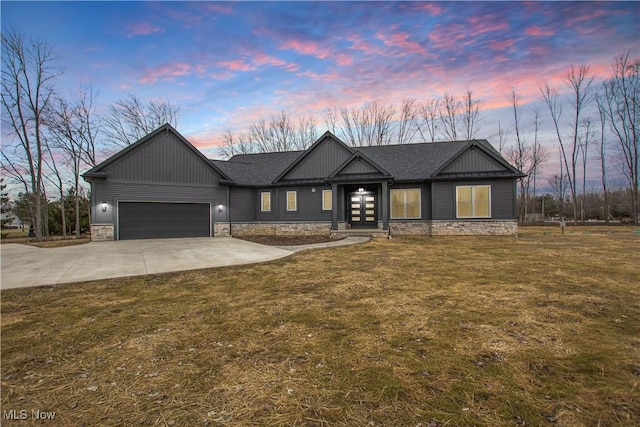 view of front of home featuring a garage, concrete driveway, stone siding, roof with shingles, and a front yard