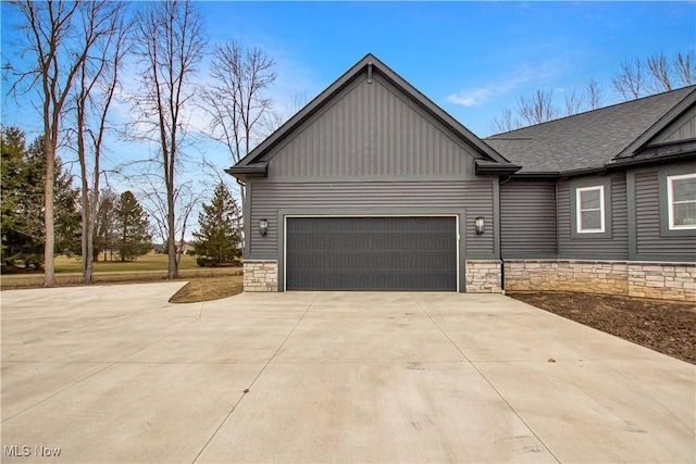 view of side of property with a garage, stone siding, board and batten siding, and concrete driveway