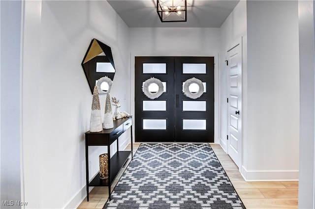 entryway featuring a notable chandelier, french doors, baseboards, and light wood-style floors