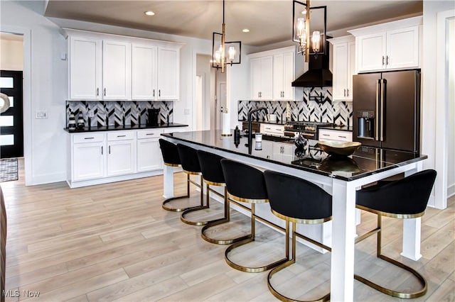 kitchen with dark countertops, wall chimney exhaust hood, light wood-style flooring, and high quality appliances