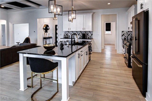 kitchen with dark countertops, white cabinetry, a sink, high end black fridge, and a kitchen bar