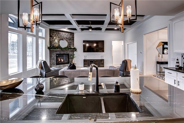 kitchen with coffered ceiling, open floor plan, dark stone countertops, a fireplace, and white cabinetry