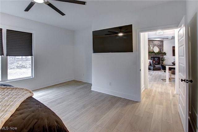 bedroom featuring a ceiling fan, a large fireplace, baseboards, and light wood finished floors