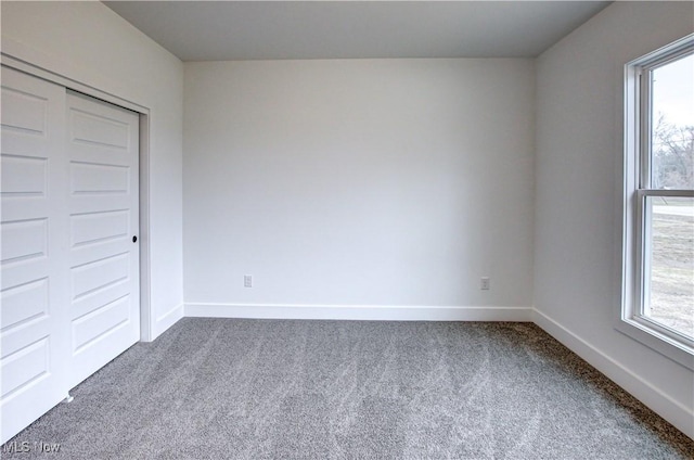 unfurnished bedroom featuring dark colored carpet, multiple windows, and baseboards