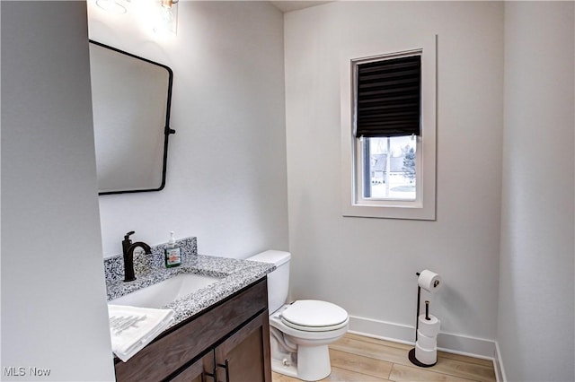 half bathroom with baseboards, vanity, toilet, and wood finished floors