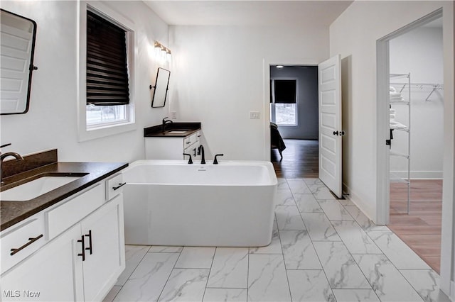 bathroom featuring a freestanding tub, two vanities, a sink, baseboards, and marble finish floor