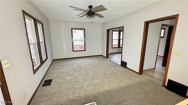 carpeted empty room featuring a textured ceiling, a ceiling fan, visible vents, and baseboards