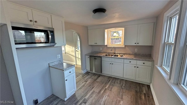 kitchen with arched walkways, white cabinets, appliances with stainless steel finishes, wood finished floors, and a sink