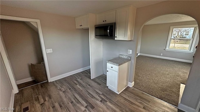 kitchen featuring arched walkways, dark wood-type flooring, stainless steel microwave, and white cabinets