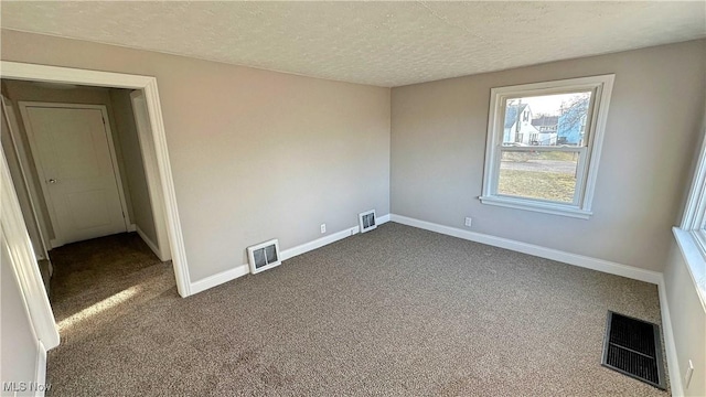 empty room featuring a textured ceiling, dark colored carpet, visible vents, and baseboards