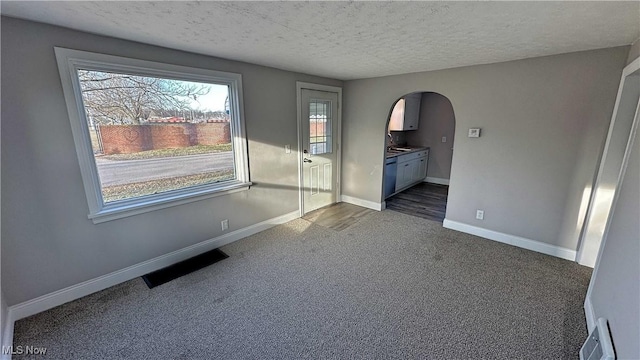 unfurnished room featuring arched walkways, visible vents, dark carpet, a textured ceiling, and baseboards