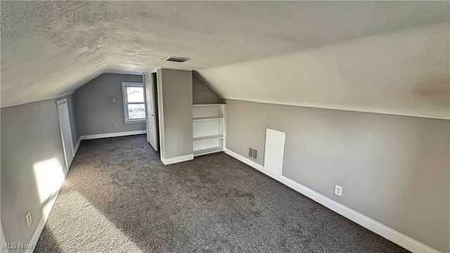 bonus room featuring lofted ceiling, visible vents, dark carpet, a textured ceiling, and baseboards