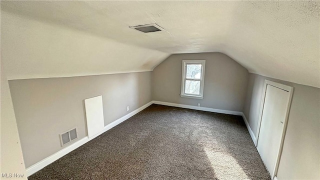 additional living space featuring baseboards, visible vents, vaulted ceiling, dark colored carpet, and a textured ceiling