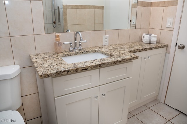 bathroom featuring toilet, vanity, tile patterned flooring, and tile walls