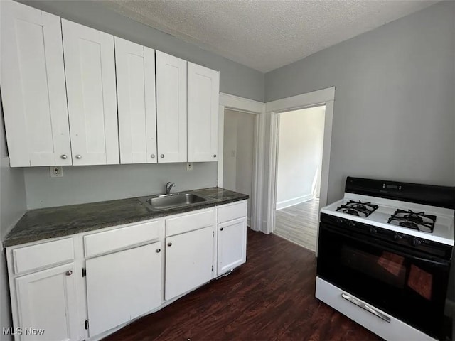 kitchen featuring dark wood-style floors, gas range oven, dark countertops, white cabinetry, and a sink