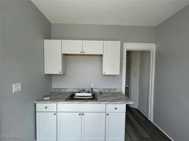 kitchen with baseboards, white cabinetry, dark wood-type flooring, and a sink