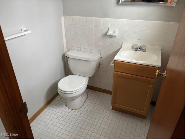 half bathroom featuring toilet, vanity, baseboards, tile walls, and tile patterned floors