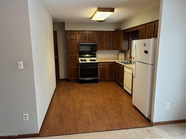 kitchen featuring white appliances, wood finished floors, a sink, light countertops, and backsplash