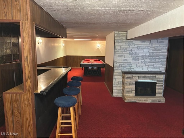 bar with wooden walls, a wainscoted wall, carpet, a textured ceiling, and a bar