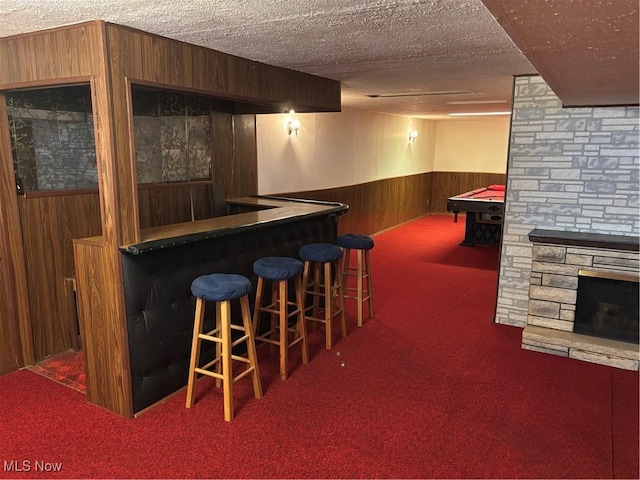 bar featuring a textured ceiling, wooden walls, a wainscoted wall, carpet floors, and a bar