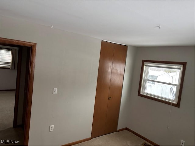 unfurnished bedroom featuring a closet, light carpet, and baseboards