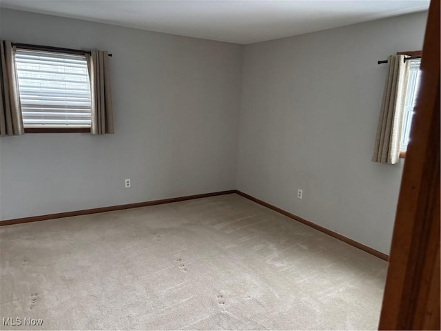 spare room featuring light carpet and baseboards