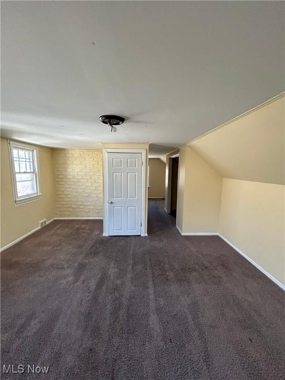 additional living space with lofted ceiling, visible vents, dark carpet, and baseboards