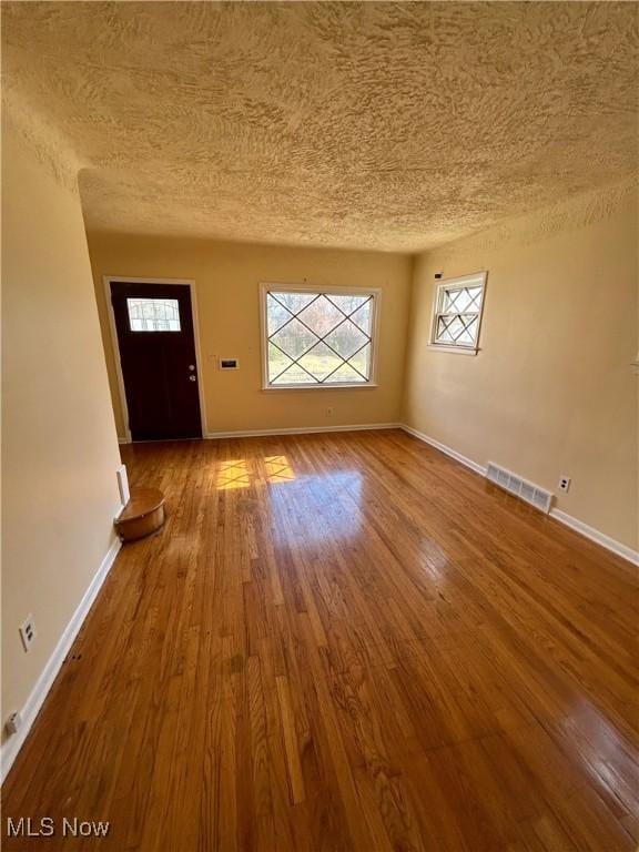 interior space featuring a textured ceiling, wood finished floors, visible vents, and baseboards