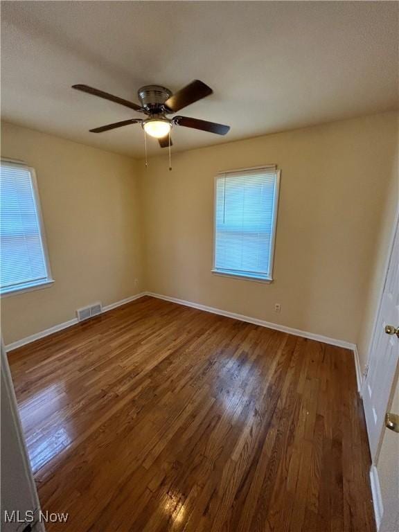 unfurnished room with baseboards, wood finished floors, visible vents, and a healthy amount of sunlight