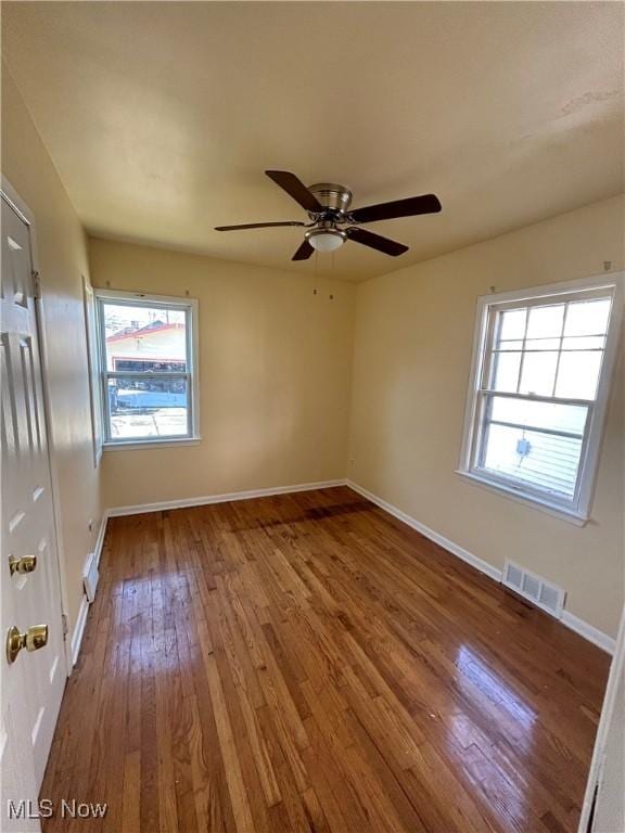 unfurnished room featuring a healthy amount of sunlight, hardwood / wood-style flooring, baseboards, and visible vents