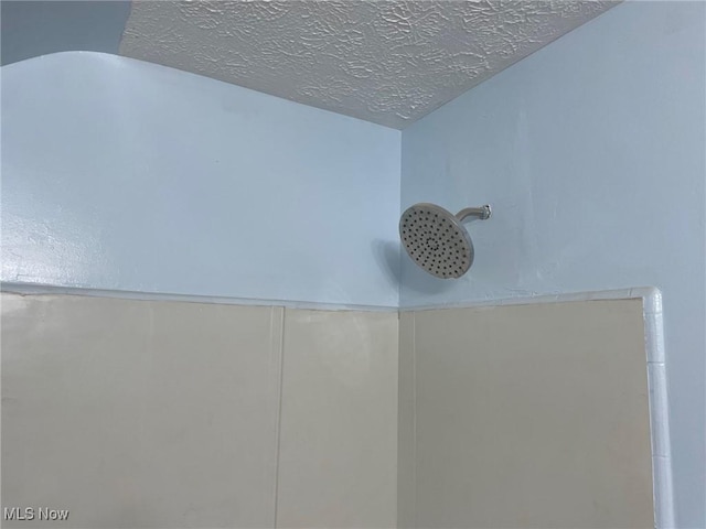 interior details featuring a textured ceiling and tiled shower