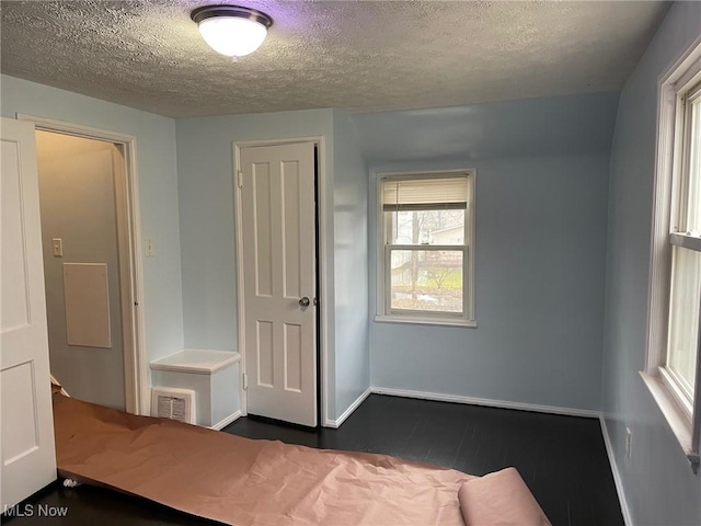 unfurnished bedroom featuring baseboards, visible vents, dark wood-type flooring, a textured ceiling, and a closet