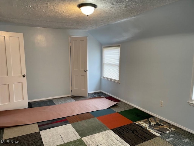 empty room with a textured ceiling, vaulted ceiling, and baseboards