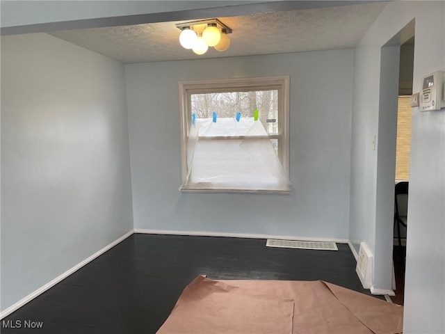 interior space with visible vents, a textured ceiling, baseboards, and wood finished floors