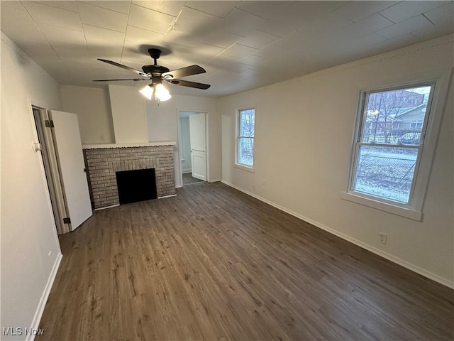 unfurnished living room featuring a brick fireplace, a ceiling fan, baseboards, and dark wood-style flooring