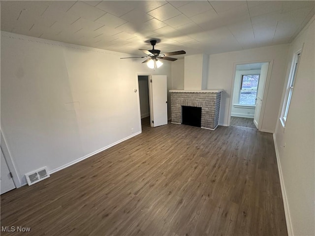 unfurnished living room with dark wood-style flooring, a ceiling fan, visible vents, baseboards, and a brick fireplace