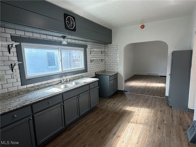 kitchen featuring dark wood-style flooring, open shelves, tasteful backsplash, gray cabinetry, and a sink